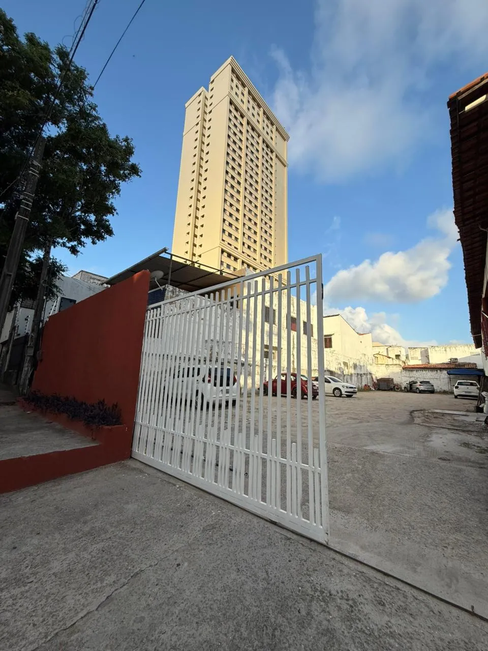 Portão do estacionamento aberto, com o pátio cheio de carros ao fundo